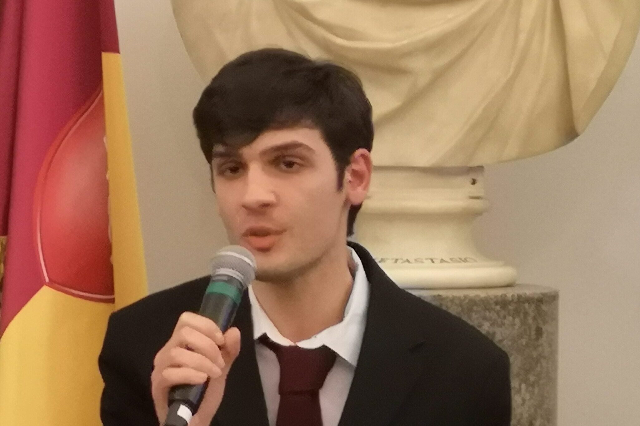Uomo in giacca parla al microfono.